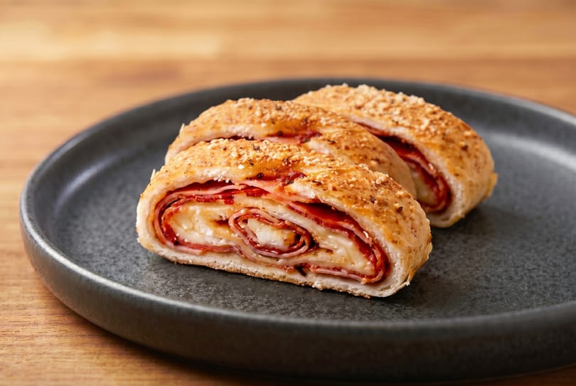 Two slices of stromboli filled with ham, pepperoni, and melted cheese on a dark plate.